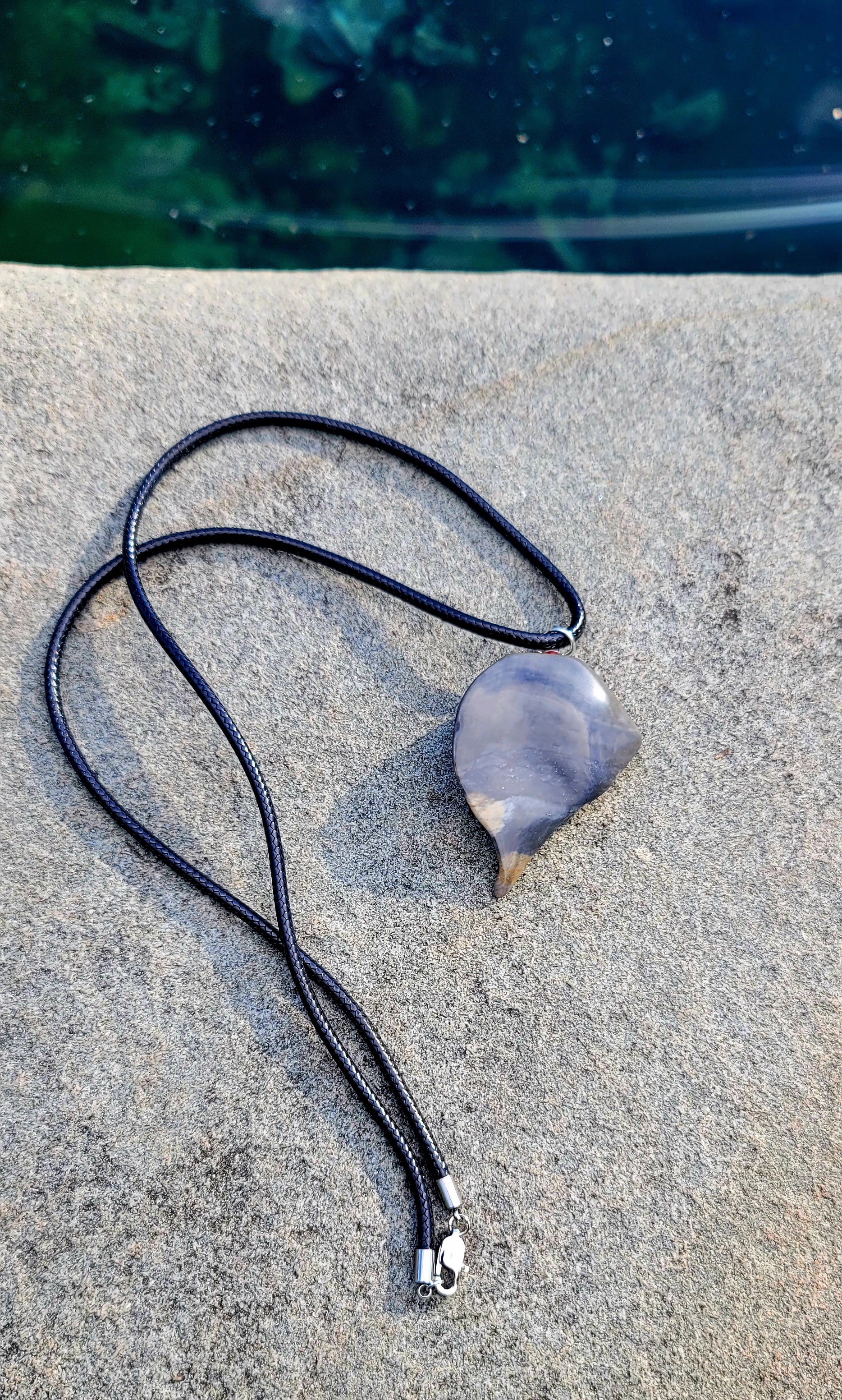 This Polychrome Jasper pendant is sure to be one of the most unique pieces you'll ever come across. Grey and White in color, it has the shape of the continent, Africa. It has stainless steel trim and black string. Pictured lying flat with front shown.