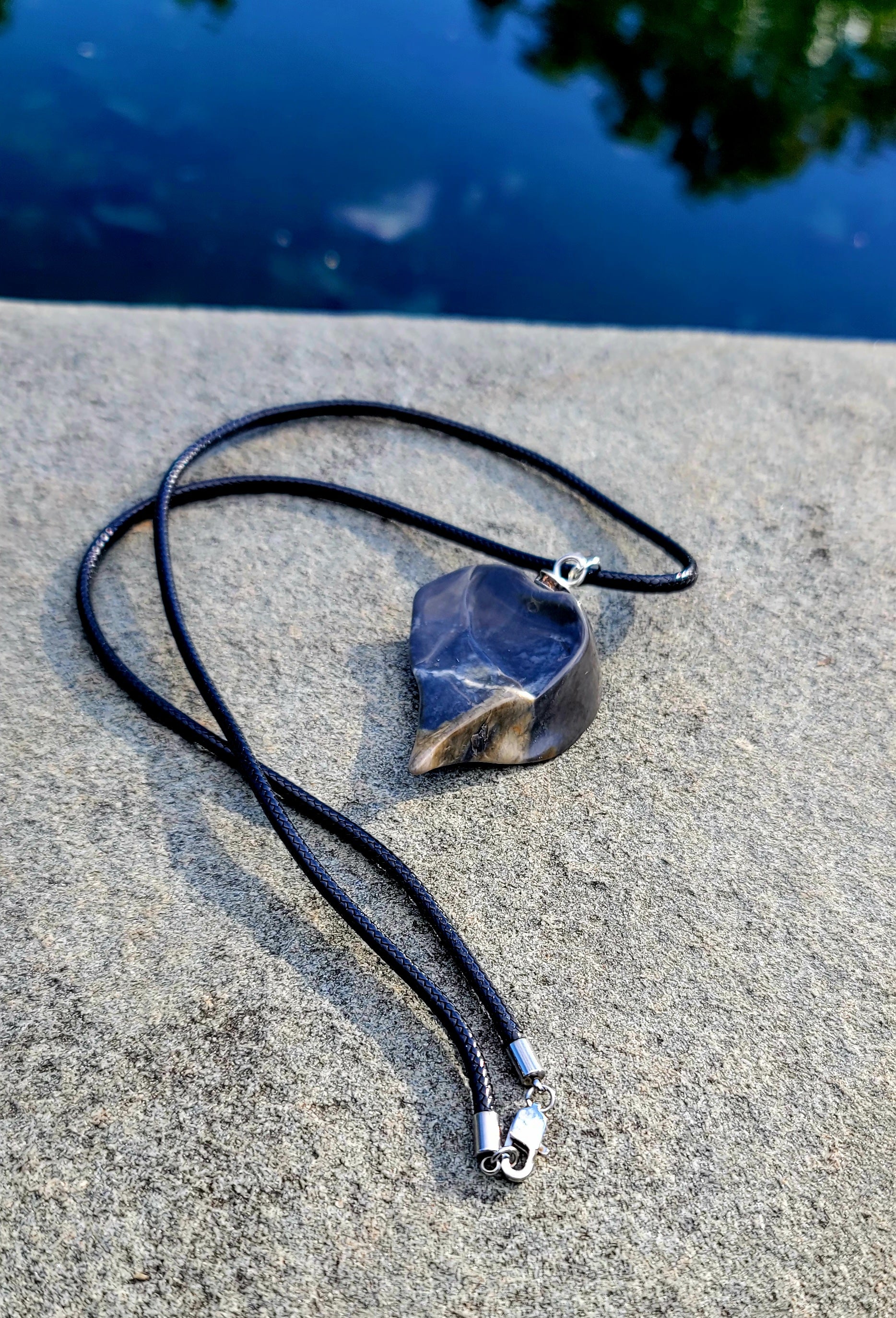 This Polychrome Jasper pendant is sure to be one of the most unique pieces you'll ever come across. Grey and White in color, it has the shape of the continent, Africa. It has stainless steel trim and black string. Pictured lying flat with back shown.