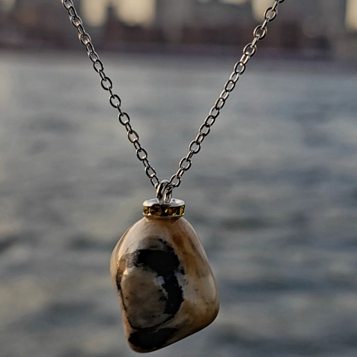 This intricately crafted zebra marble gemstone pendant is a one-of-a-kind masterpiece. Meticulously cut and polished to create an elegant pattern of black, yellow and white striped patterns. This pendant is trimmed with a stainless steel, 20" chain.