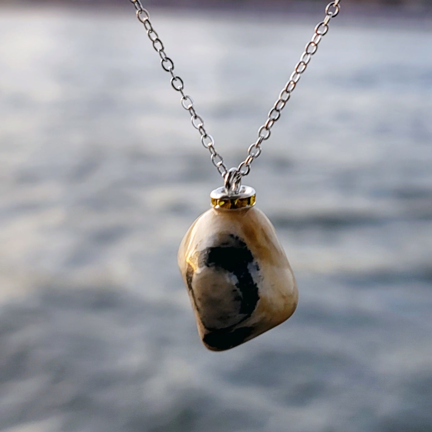 This intricately crafted zebra marble gemstone pendant is a one-of-a-kind masterpiece. Meticulously cut and polished to create an elegant pattern of black, yellow and white striped patterns. This pendant is trimmed with a stainless steel, 20" chain.