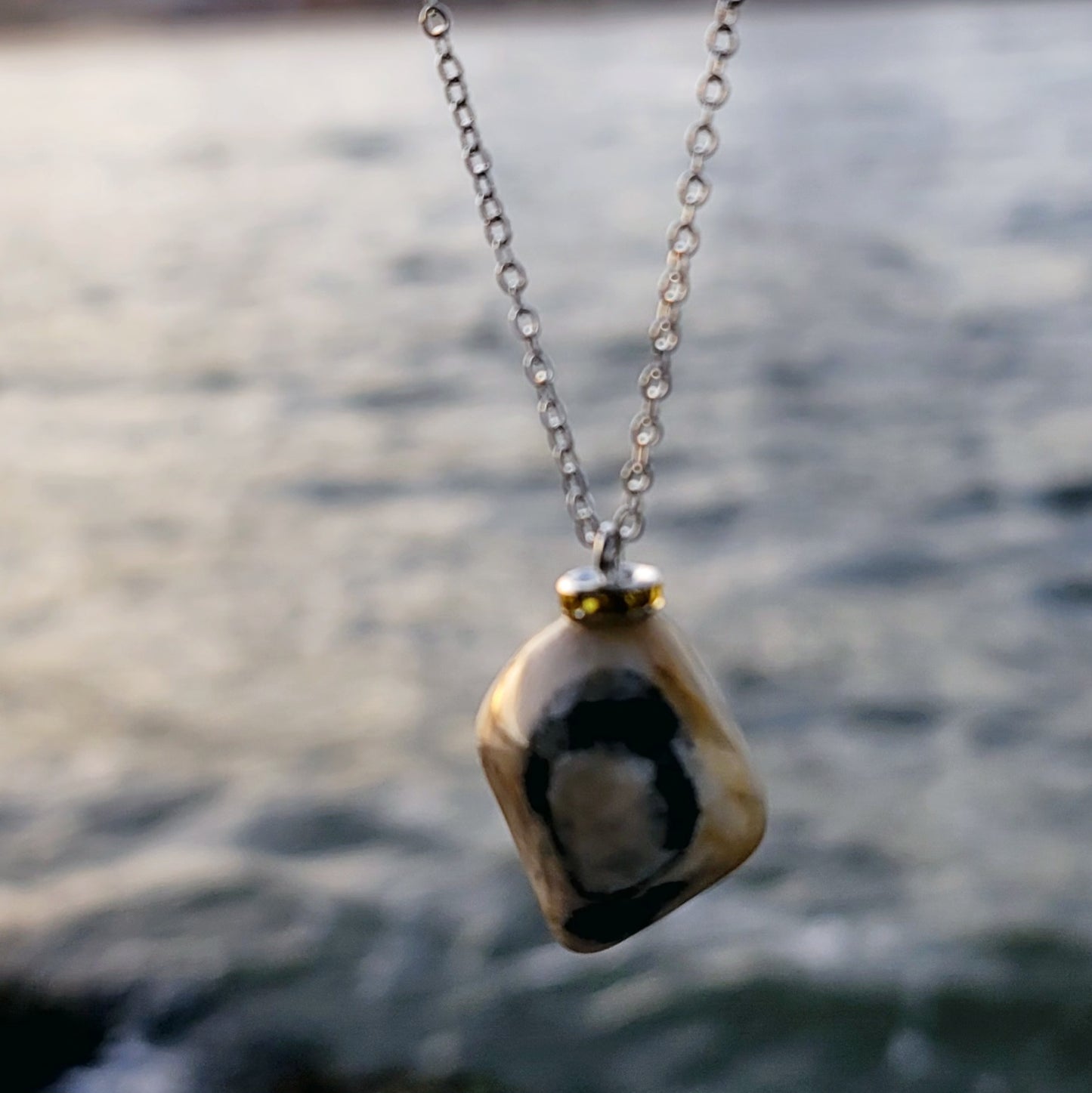 This intricately crafted zebra marble gemstone pendant is a one-of-a-kind masterpiece. Meticulously cut and polished to create an elegant pattern of black, yellow and white striped patterns. This pendant is trimmed with a stainless steel, 20" chain.