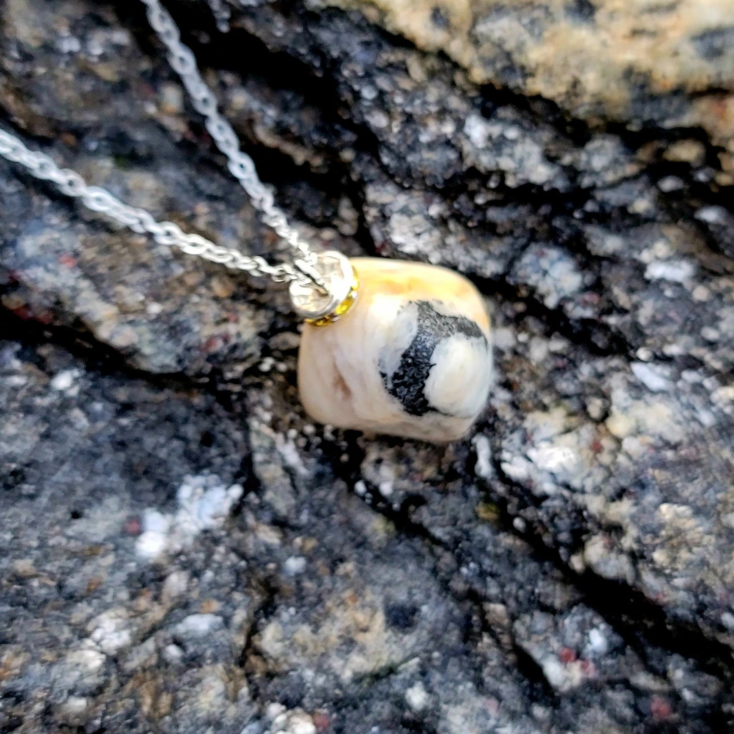 This intricately crafted zebra marble gemstone pendant is a one-of-a-kind masterpiece. Meticulously cut and polished to create an elegant pattern of black, yellow and white striped patterns. This pendant is trimmed with a stainless steel, 20" chain.