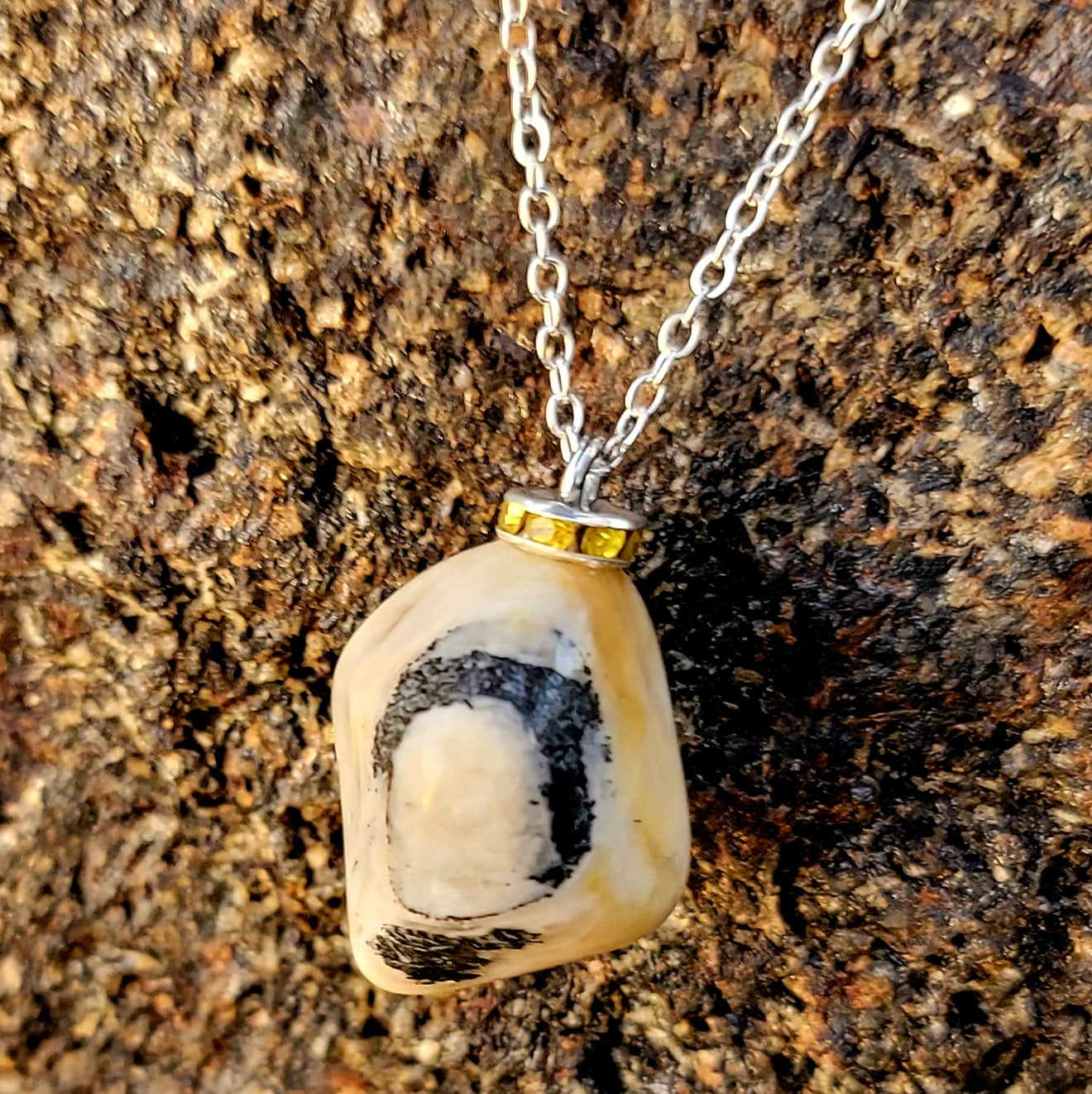 This intricately crafted zebra marble gemstone pendant is a one-of-a-kind masterpiece. Meticulously cut and polished to create an elegant pattern of black, yellow and white striped patterns. This pendant is trimmed with a stainless steel, 20" chain.