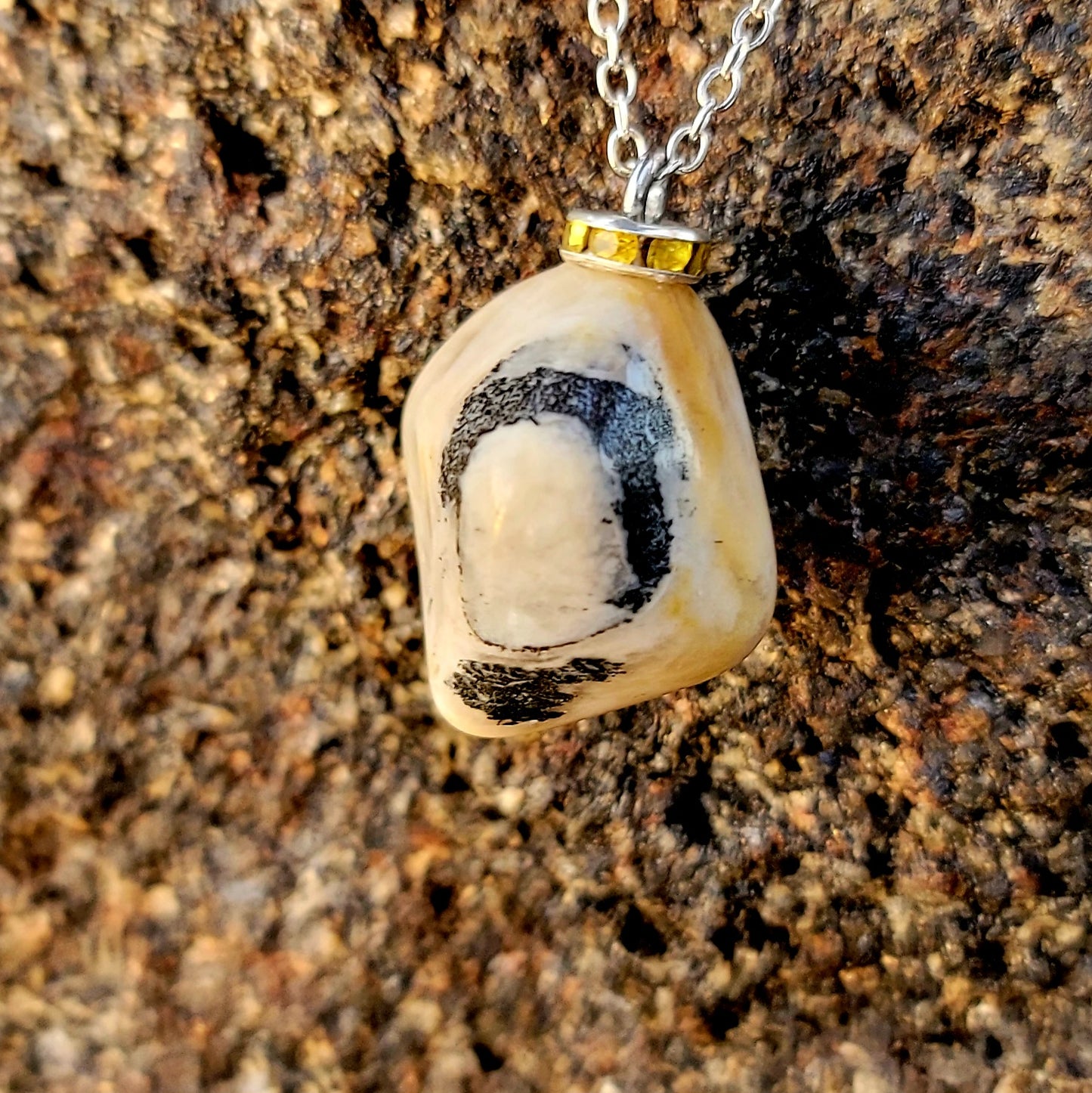 This intricately crafted zebra marble gemstone pendant is a one-of-a-kind masterpiece. Meticulously cut and polished to create an elegant pattern of black, yellow and white striped patterns. This pendant is trimmed with a stainless steel, 20" chain.