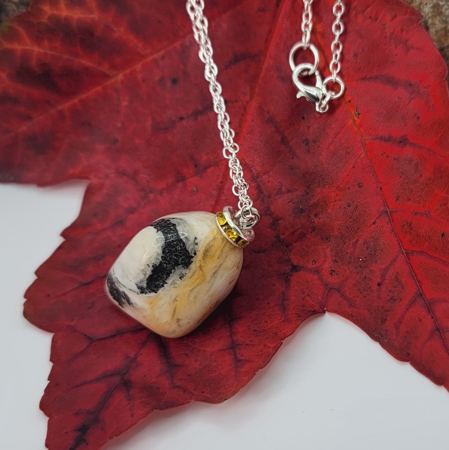 This intricately crafted zebra marble gemstone pendant is a one-of-a-kind masterpiece. Meticulously cut and polished to create an elegant pattern of black, yellow and white striped patterns. This pendant is trimmed with a stainless steel, 20" chain.