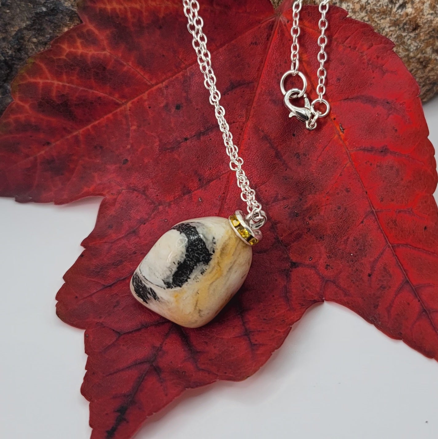 This intricately crafted zebra marble gemstone pendant is a one-of-a-kind masterpiece. Meticulously cut and polished to create an elegant pattern of black, yellow and white striped patterns. This pendant is trimmed with a stainless steel, 20" chain.