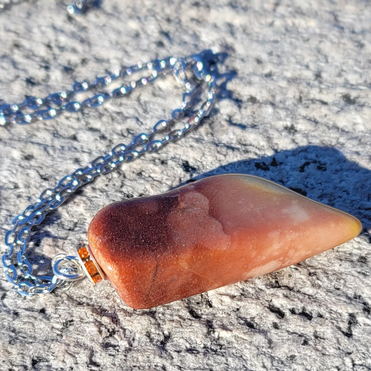 Gorgeous Multi-colored Mookaite Jasper Pendant. This pendant has deep hues of rich colors, such as Reds, Oranges, Browns and Yellow. It is trimmed with a 20" Silver-plated chain. This is a beautiful and very unique piece that is also perfect as a gift