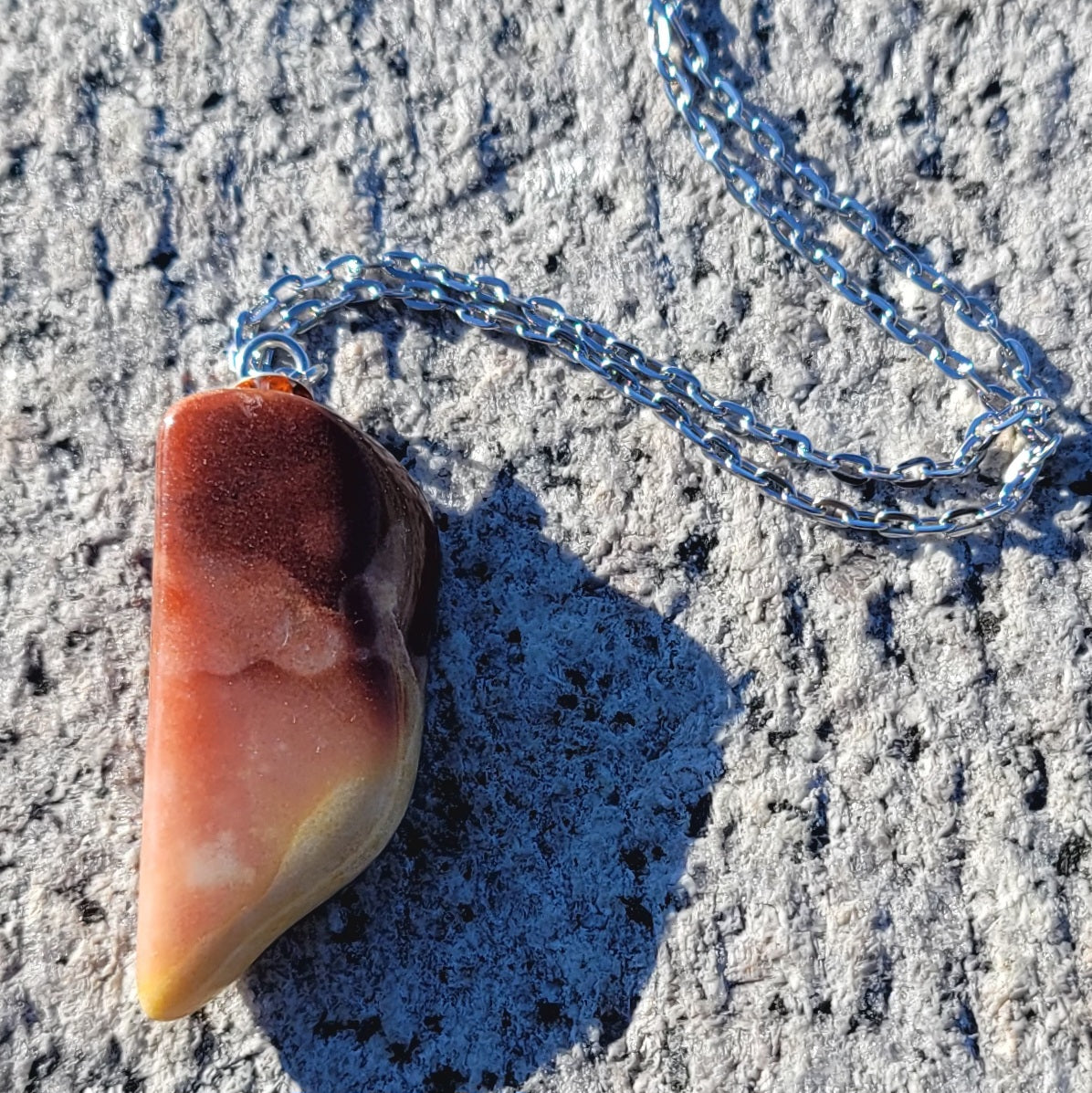 Gorgeous Multi-colored Mookaite Jasper Pendant. This pendant has deep hues of rich colors, such as Reds, Oranges, Browns and Yellow. It is trimmed with a 20" Silver-plated chain. This is a beautiful and very unique piece that is also perfect as a gift