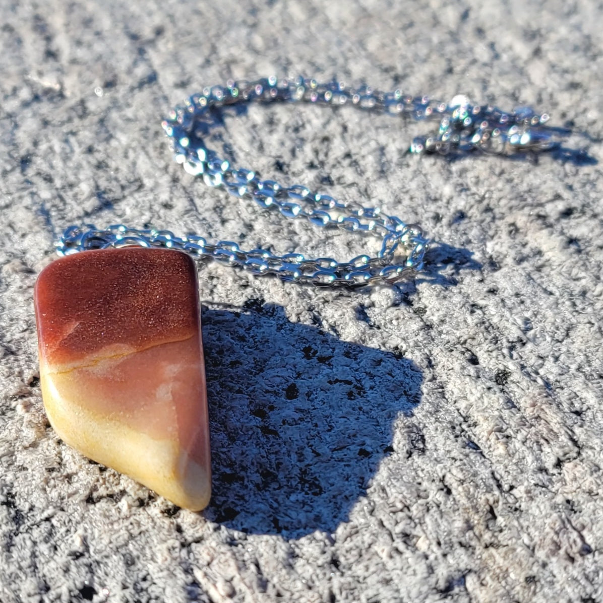 Gorgeous Multi-colored Mookaite Jasper Pendant. This pendant has deep hues of rich colors, such as Reds, Oranges, Browns and Yellow. It is trimmed with a 20" Silver-plated chain. This is a beautiful and very unique piece that is also perfect as a gift