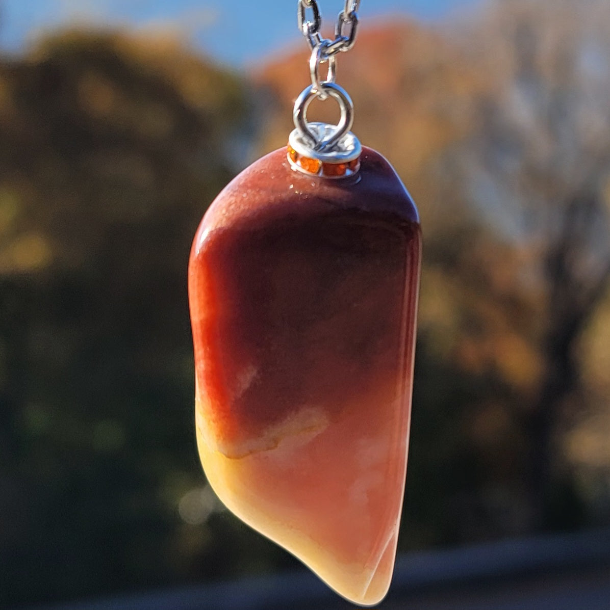 Gorgeous Multi-colored Mookaite Jasper Pendant. This pendant has deep hues of rich colors, such as Reds, Oranges, Browns and Yellow. It is trimmed with a 20" Silver-plated chain. This is a beautiful and very unique piece that is also perfect as a gift