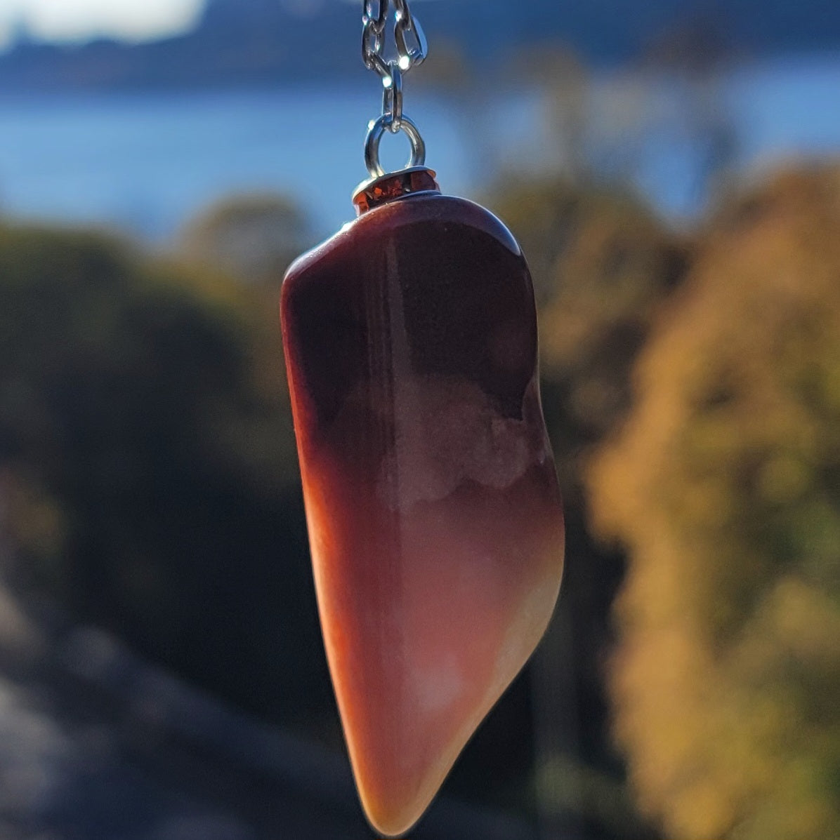 Gorgeous Multi-colored Mookaite Jasper Pendant. This pendant has deep hues of rich colors, such as Reds, Oranges, Browns and Yellow. It is trimmed with a 20" Silver-plated chain. This is a beautiful and very unique piece that is also perfect as a gift