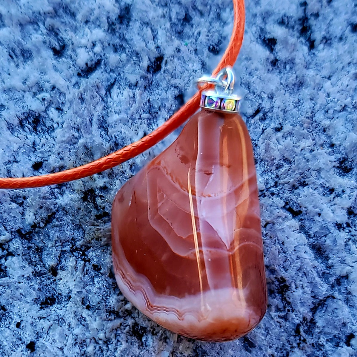 Beautiful Carnelian Agate Pendant with intriguing colors and patterns. It is trimmed with stainless steel findings and an 18" Polyester string.