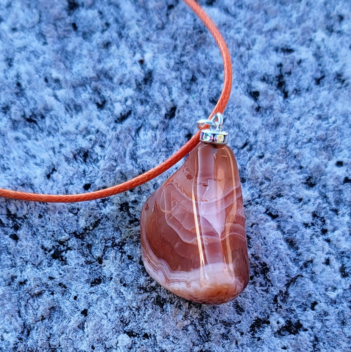 Beautiful Carnelian Agate Pendant with intriguing colors and patterns. It is trimmed with stainless steel findings and an 18" Polyester string.