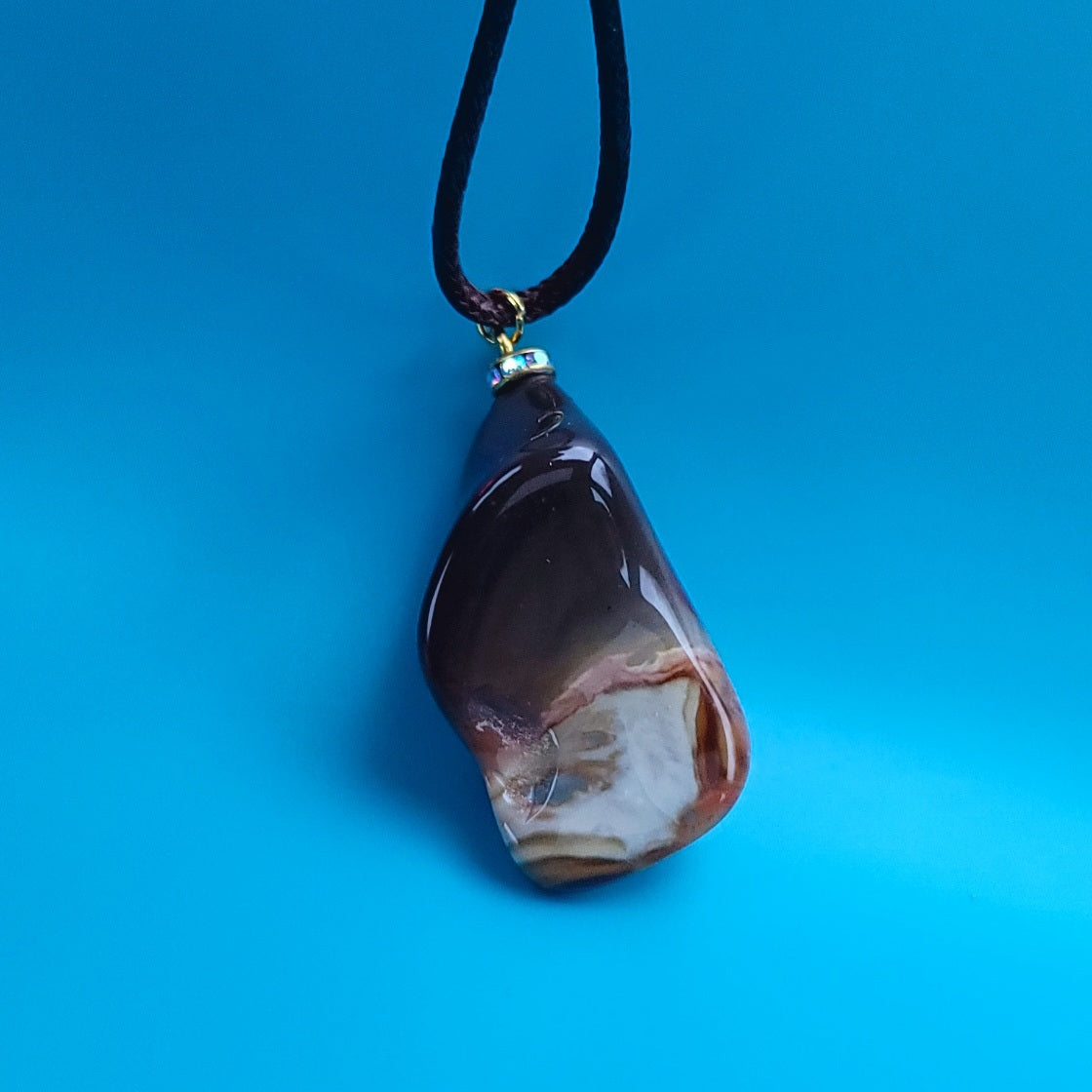 Amazing Desert Jasper Pendant with a very unique shape and an intriguing array of colors. Trimmed with stainless steel findings and a Brown Polyester string.