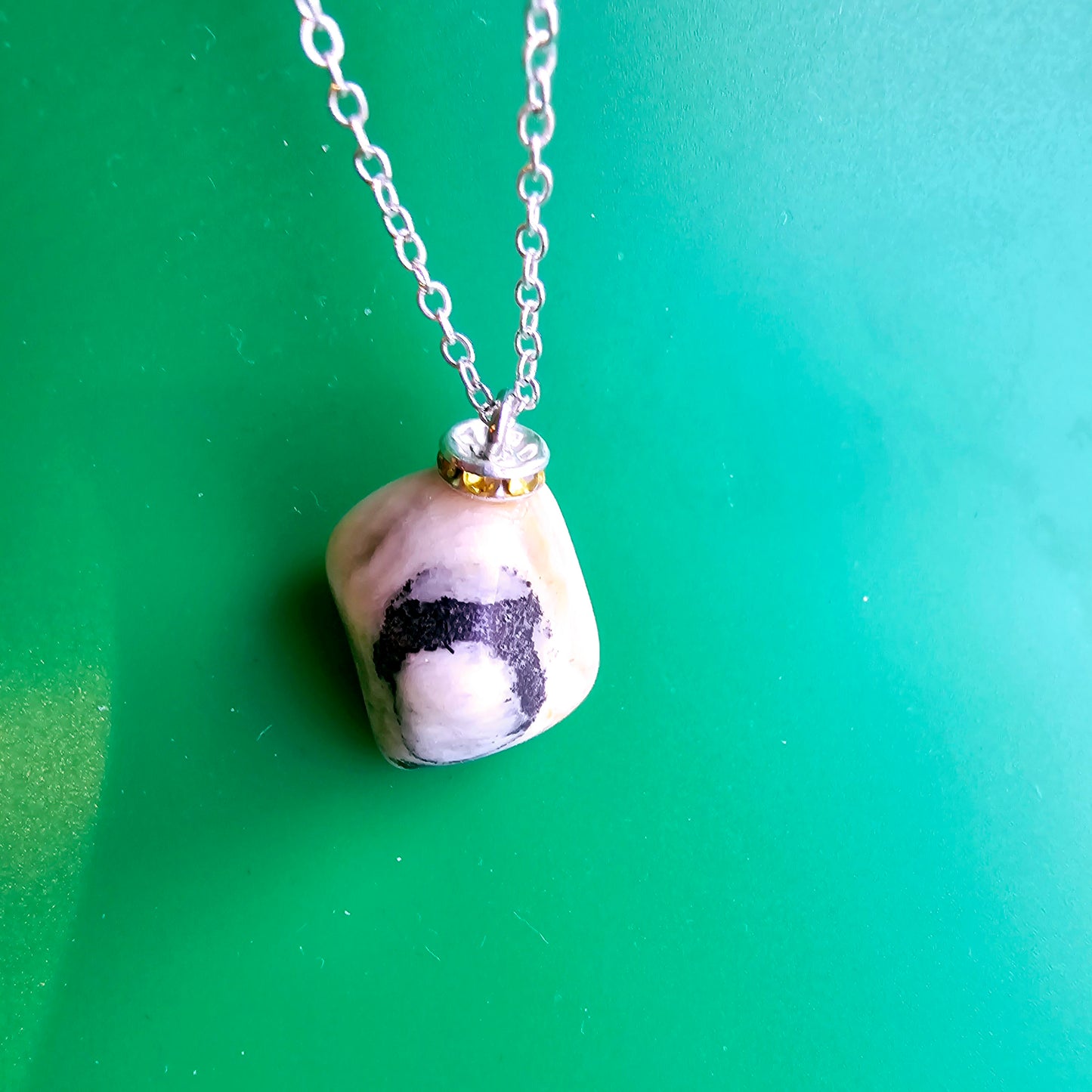 This intricately crafted zebra marble gemstone pendant is a one-of-a-kind masterpiece. Meticulously cut and polished to create an elegant pattern of black, yellow and white striped patterns. This pendant is trimmed with a stainless steel, 20" chain.