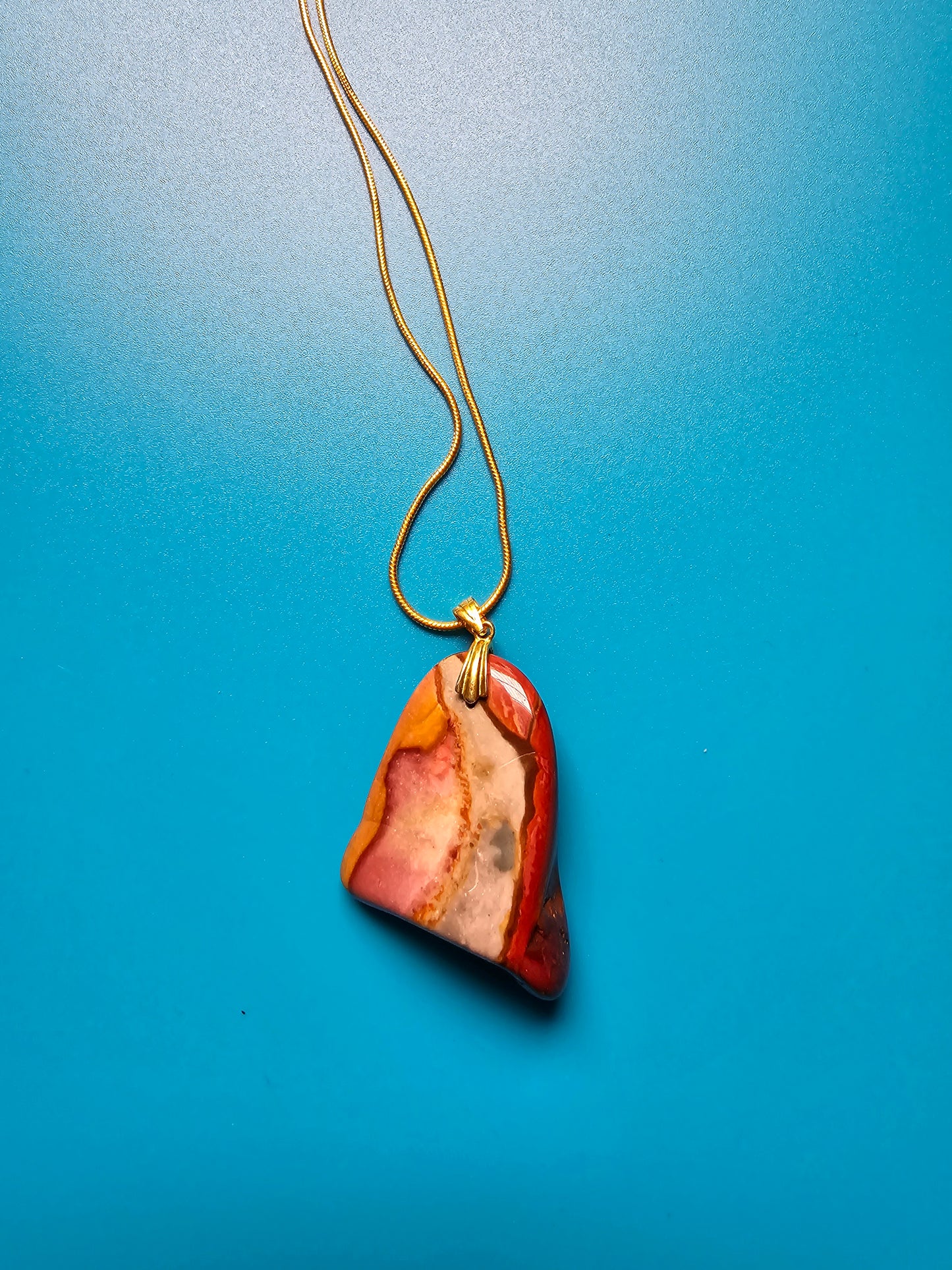 A stunning beauty of our Desert Jasper Pendant. This unique stone features a mesmerizing color pattern and is known for its powerful metaphysical properties. It promotes inner peace, balance and protection while enhancing creativity and self-expression. Pictured on a Blue background.