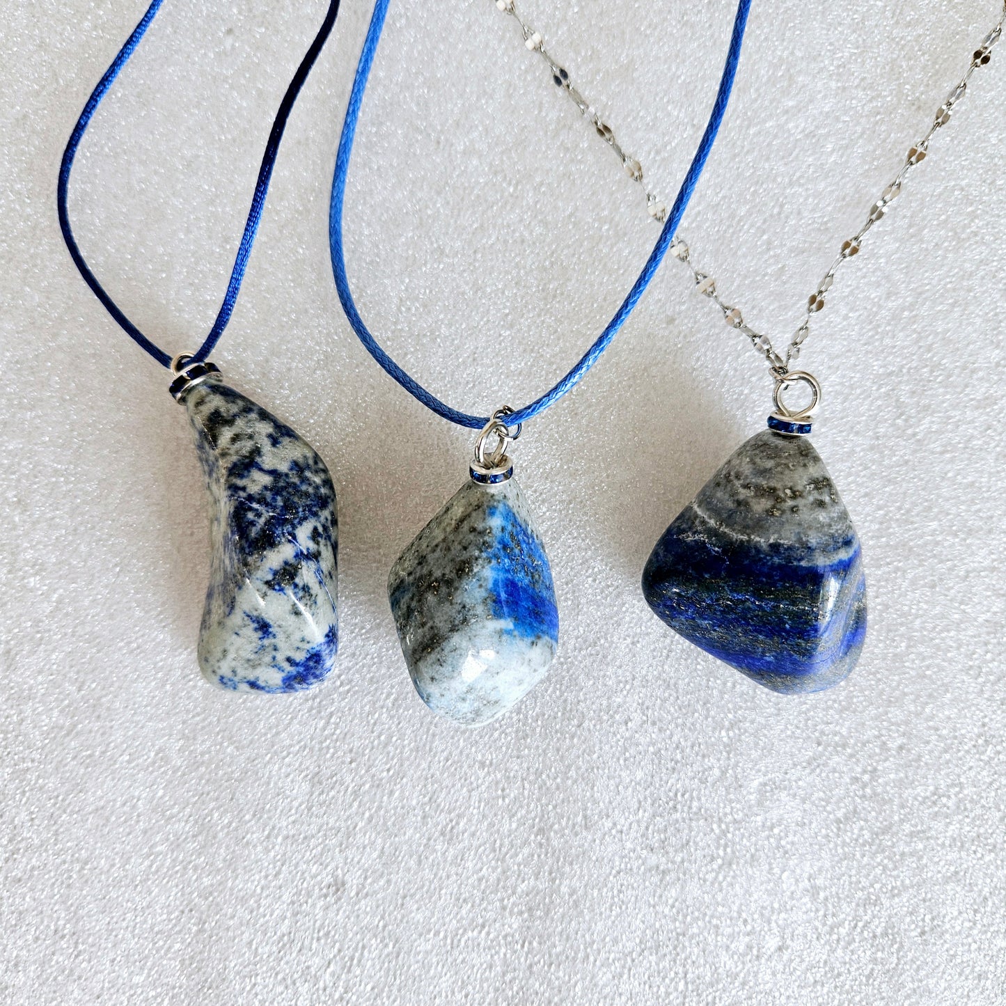 Striking Lapis Lazuli Pendant with deep hues of Blue and Greys. It is trimmed with Silver-Plated findings and a 20" sterling Silver chain. Pictured with two other Laps Lazuli pendants.