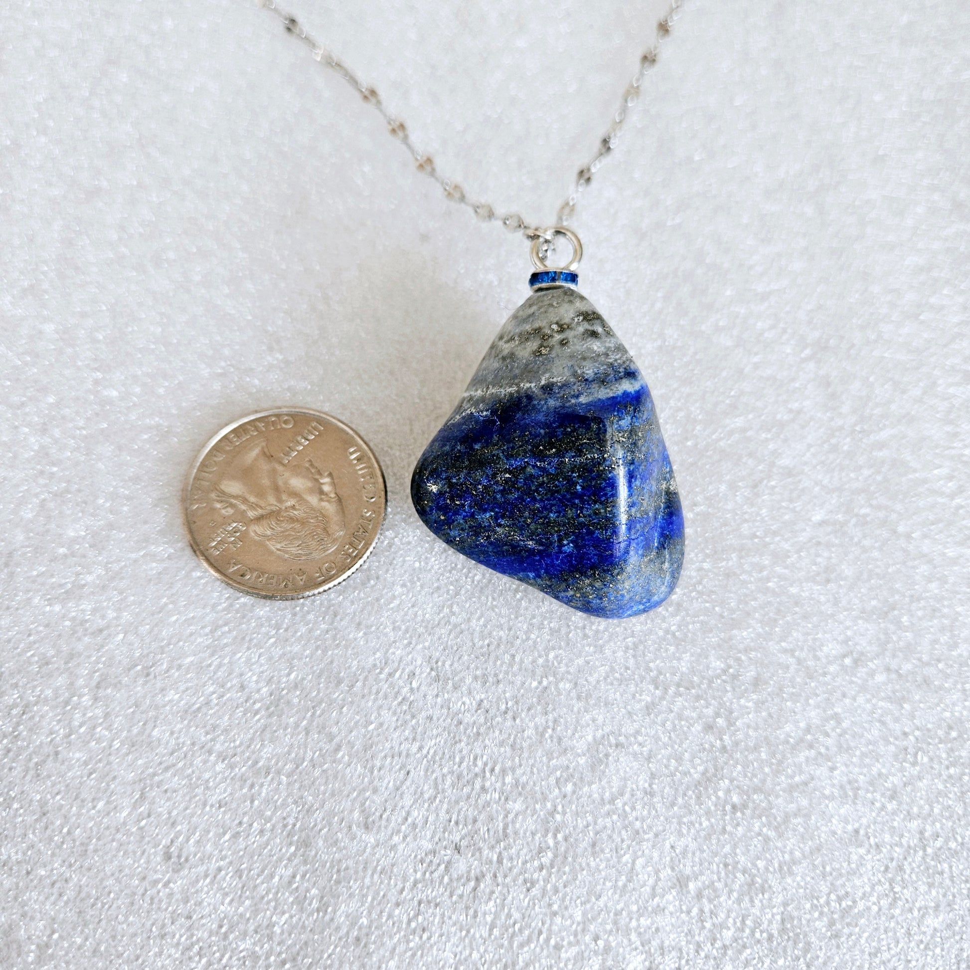 Striking Lapis Lazuli Pendant with deep hues of Blue and Greys. It is trimmed with Silver-Plated findings and a 20" sterling Silver chain. Shown compared to a quarter for size reference.